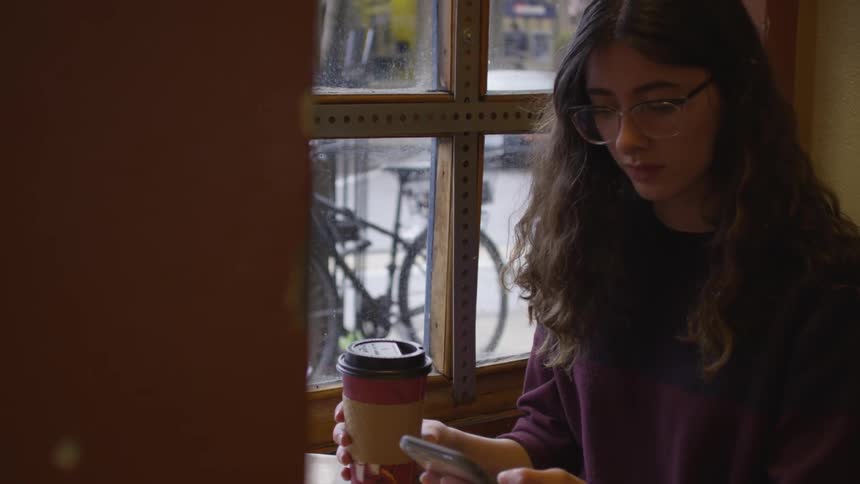 A woman tapping on her phone while holding a cup of coffee