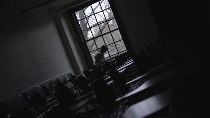 A student sits in an empty classroom near the large window