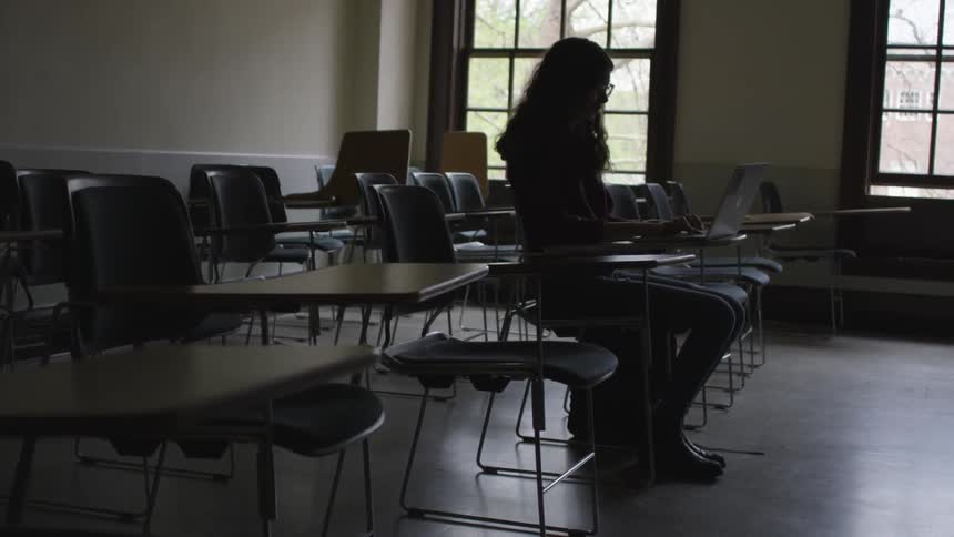 Girl works at a laptop in a classroom surrounded by empty desks