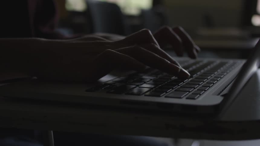 A person in a sweater types on a laptop on a desk