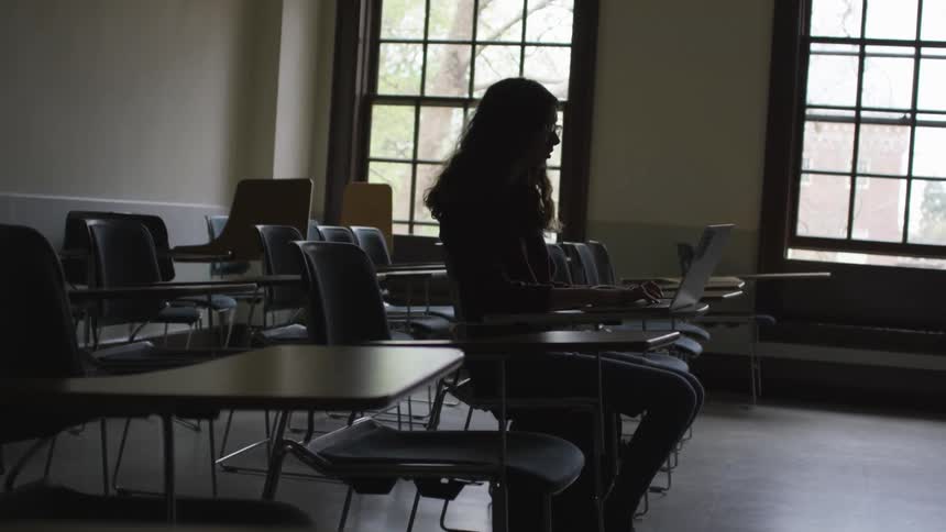 Girl sitting at a desk in a classroom working on a laptop