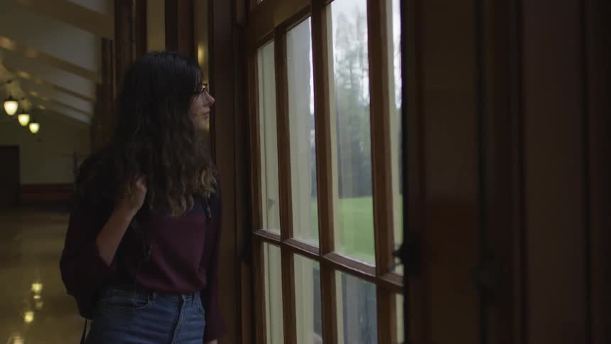 A female student looking out of a large window during the day