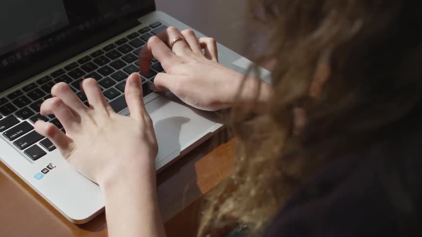 Woman sits at table typing on laptop