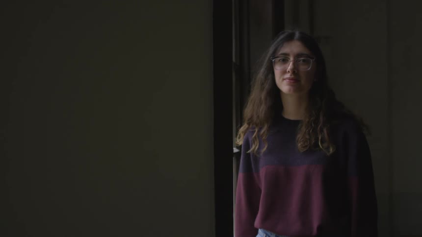 A bespectacled young brunette turns away from a georgian window