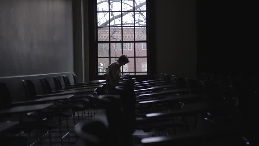 A man sits at a row of desks in a dark classroom