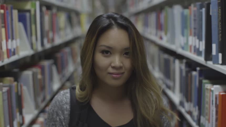 A young woman looks up from the floor as she stands between two aisles in a library