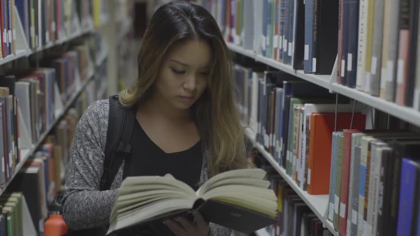 Woman pages through a book in a library aisle