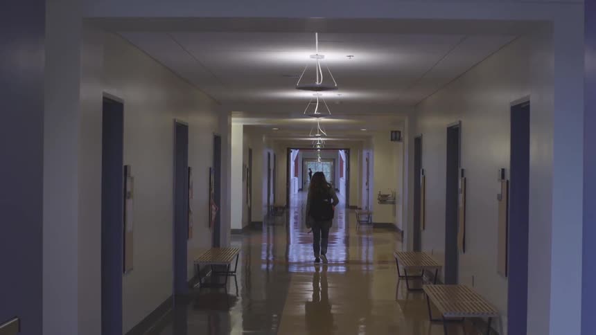 A girl walks down a school hallway lined with benches