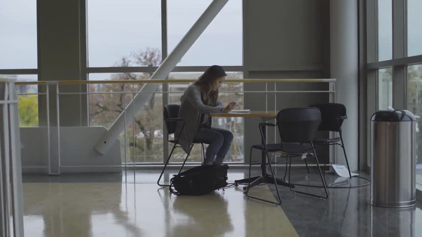 A girl sits at a table in front of windows while studying
