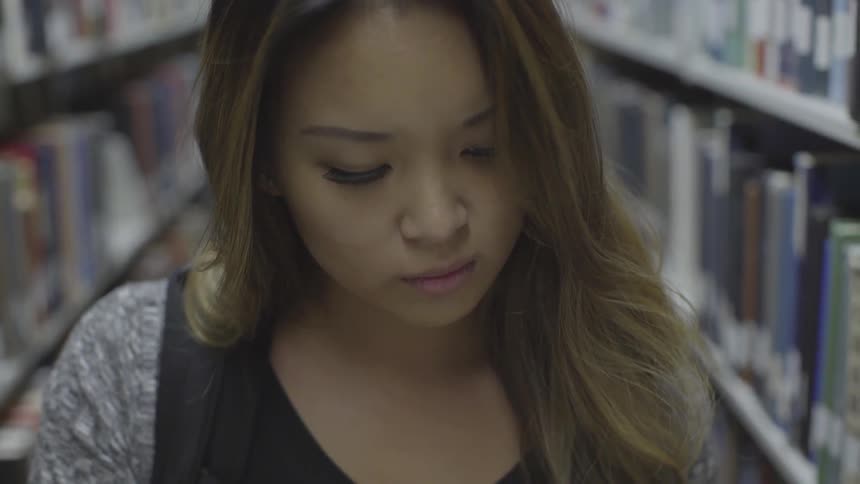 Woman looks through a book standing in an aisle at the library