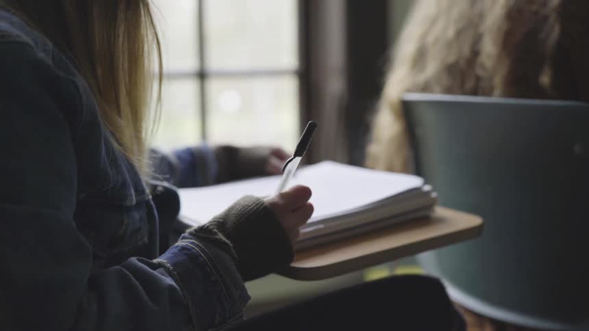 Student writes in a notebook while sitting at a desk