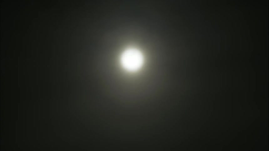 Clouds pass over a full glowing moon in a black sky