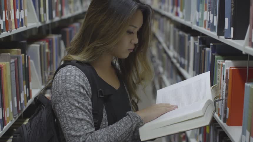 Woman reading a book she took from a library bookshelf