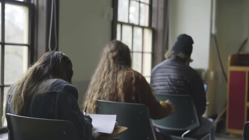 Classroom of students sit at desks writing