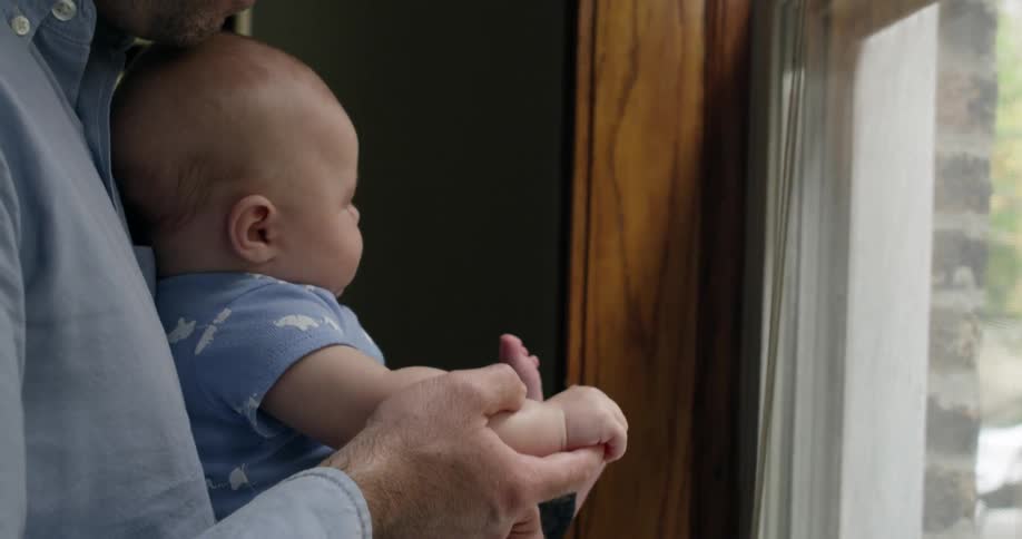 A man holds a baby in front of a window