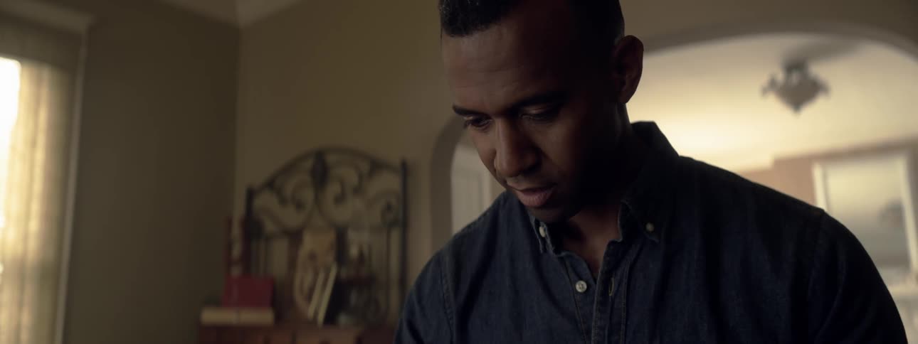 Black man looks down at something in house