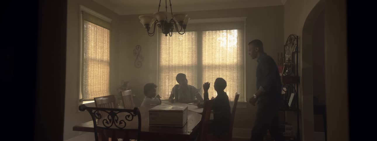 A dad walks into the dining room where his wife and two children are sitting