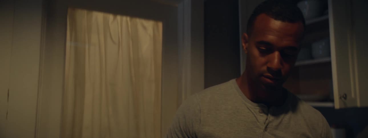 A man standing in a dimly lit kitchen takes something out of the cupboard