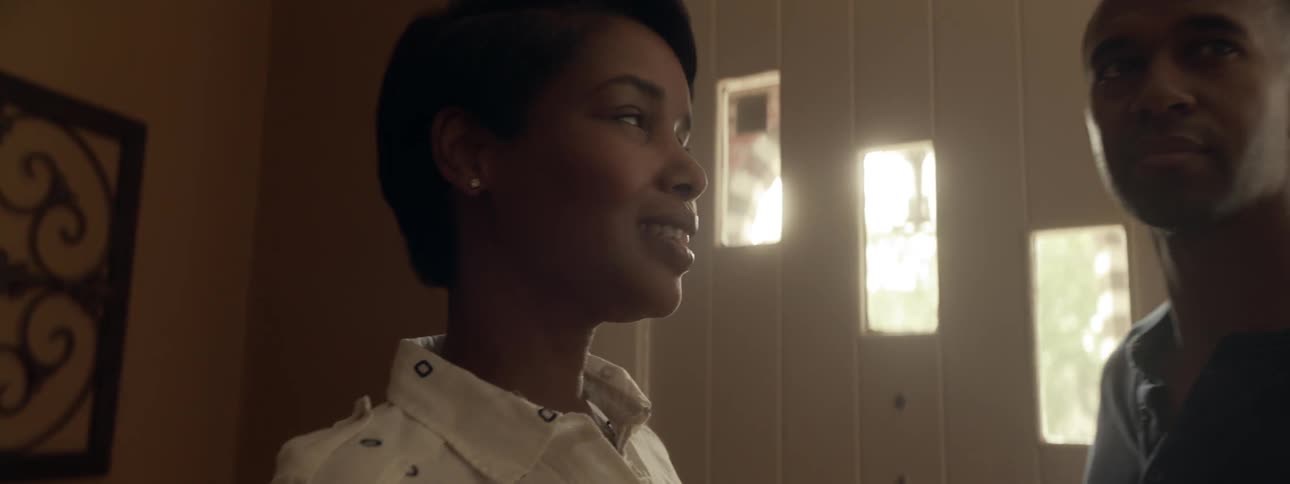 A young couple shut the front door of a house and smile as light streams through the panes of glass on the door