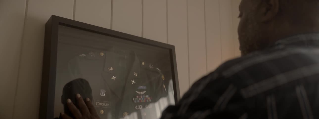 An older man is looking at a military uniform in a glass case mounted on a wall