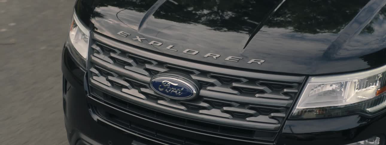 The front end of a black ford explorer as it passes parked cars on a road