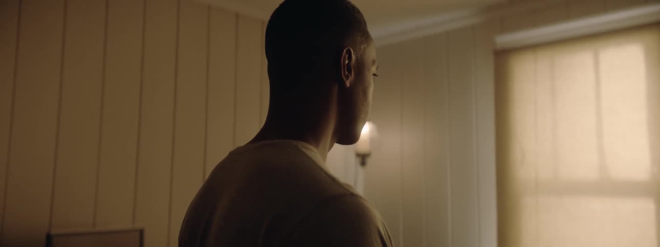 A man walks into a room toward a window then pauses and looks around