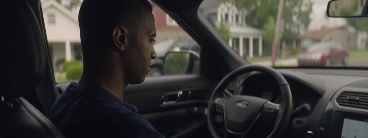 A black man sitting in a ford vehicle parked in a residential area during the day