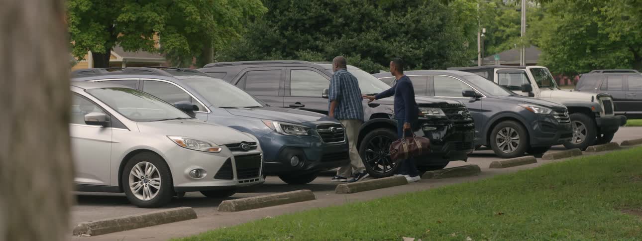 A man carries a gym bag and helps an elderly man with a cane walk to a black suv