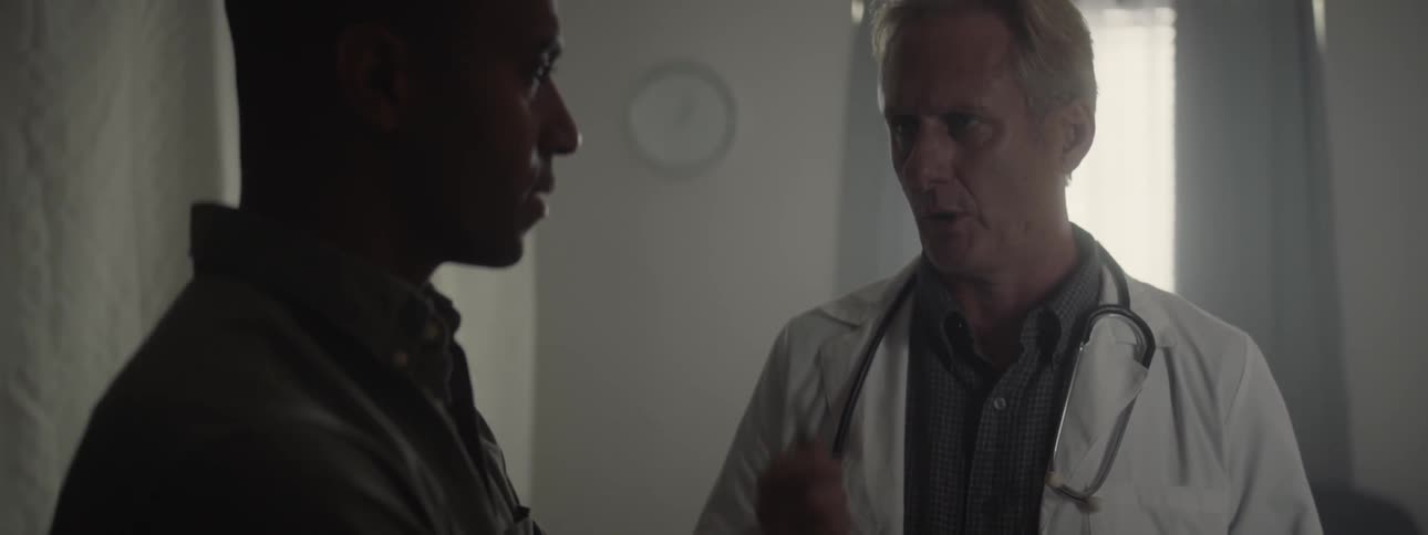 A doctor talks to a man in a room lit by sun coming through the window