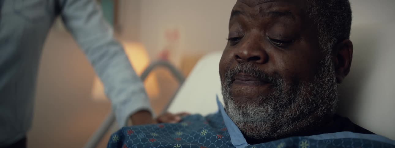 Elderly man has his shoulder rubbed by another person as he lays in a hospital bed