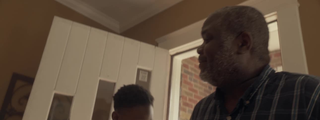 An elderly man walks into a house greeted by his family