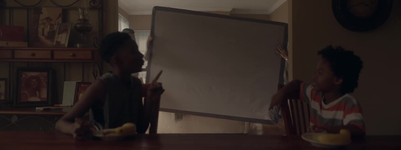 People carry a mattress while two children sit at a table