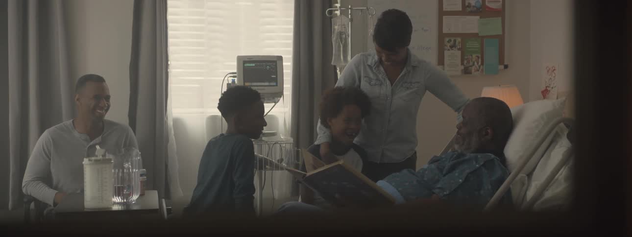 Family looks at a book with an elderly man in a hospital bed