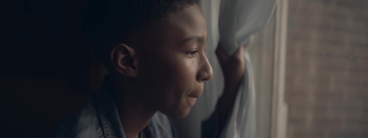 A young boy is looking out a window with anticipation or concern