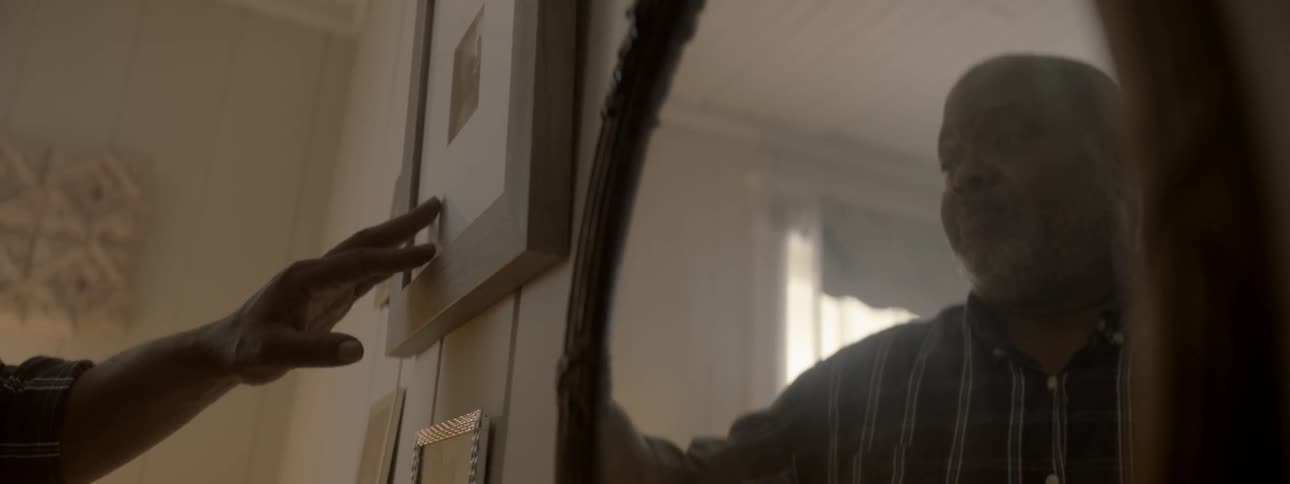 A sad man softly touches a framed photograph hanging on a wall