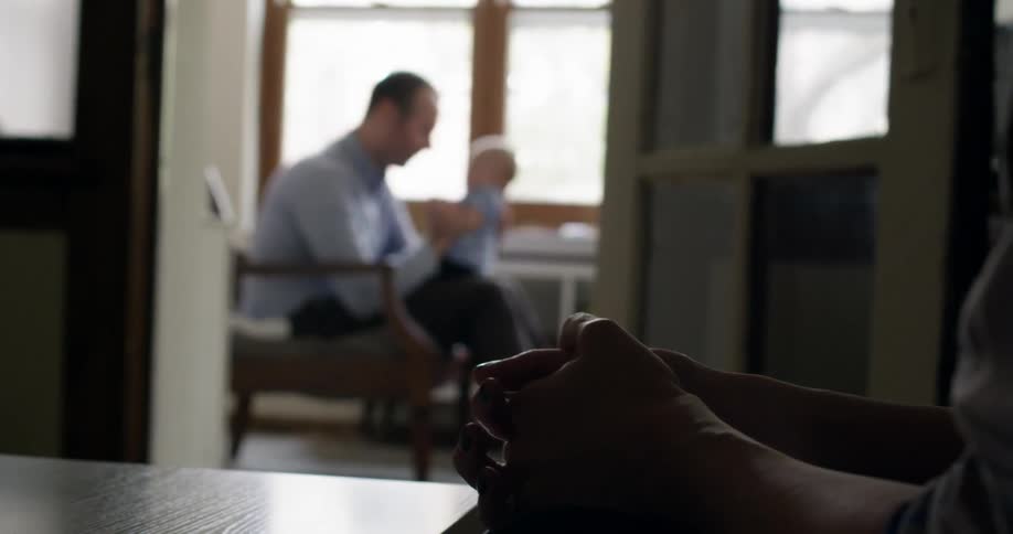 A man holds a baby while seating by a window