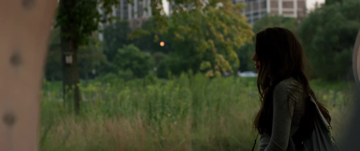 A woman standing still near a park with high rises in the background