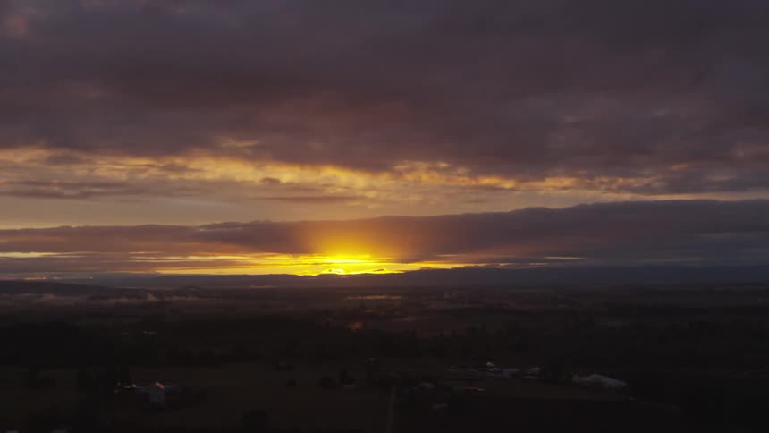 The sun glows bright yellow as it rises on the horizon over a rural area