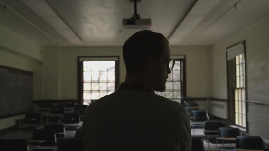 A man stands at the front of an empty classroom and looks around