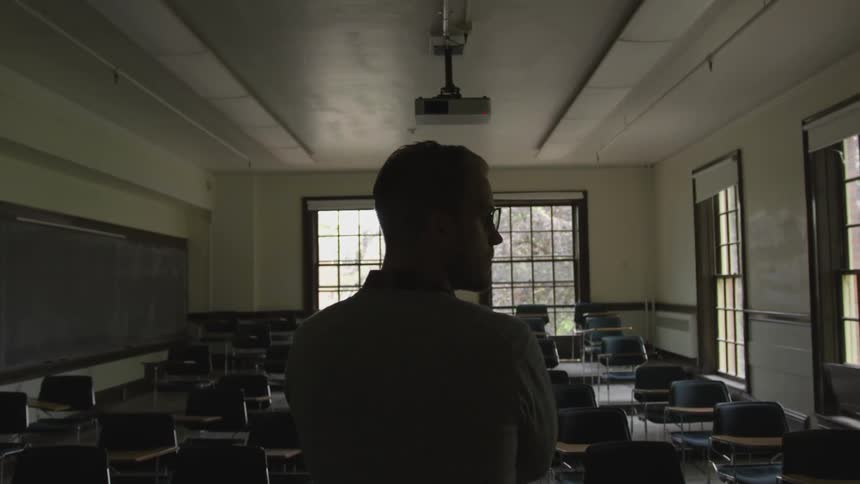 Teacher stands in dimly lit empty classroom
