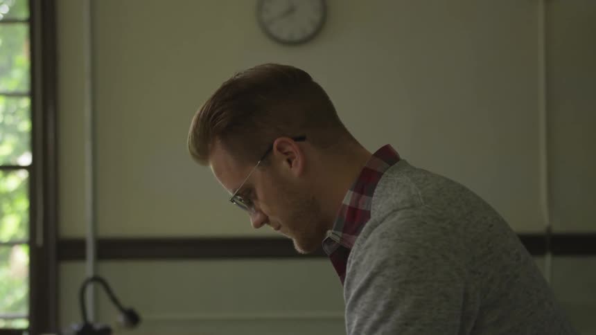 A blonde man with spectacles standing in front of a blackboard
