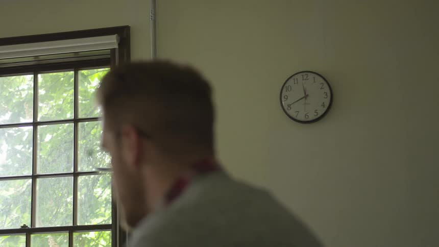 The camera focuses on a clock while a man talks to someone out of frame