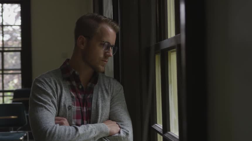 A young man in an sunlit room looks out of the window