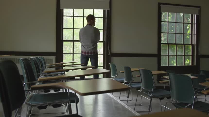 Man in classroom stands at window looking out