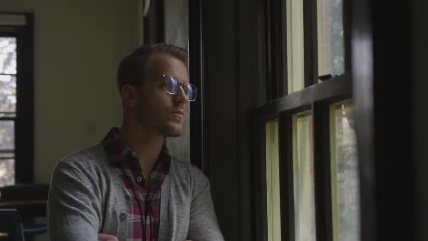 Man in cardigan looks out window