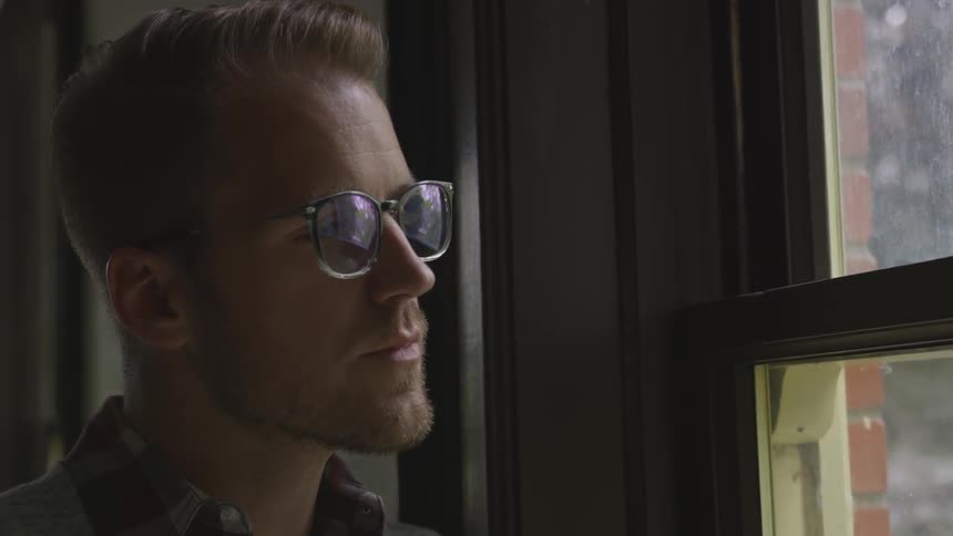 A man with glasses and a beard staring out of a window