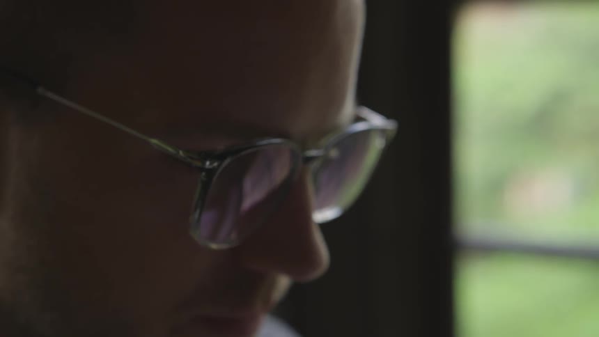 Man in glasses looks at something in front of him and slightly down