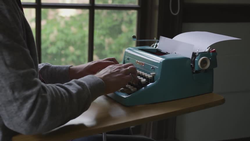 A man typing on a typewriter at a desk