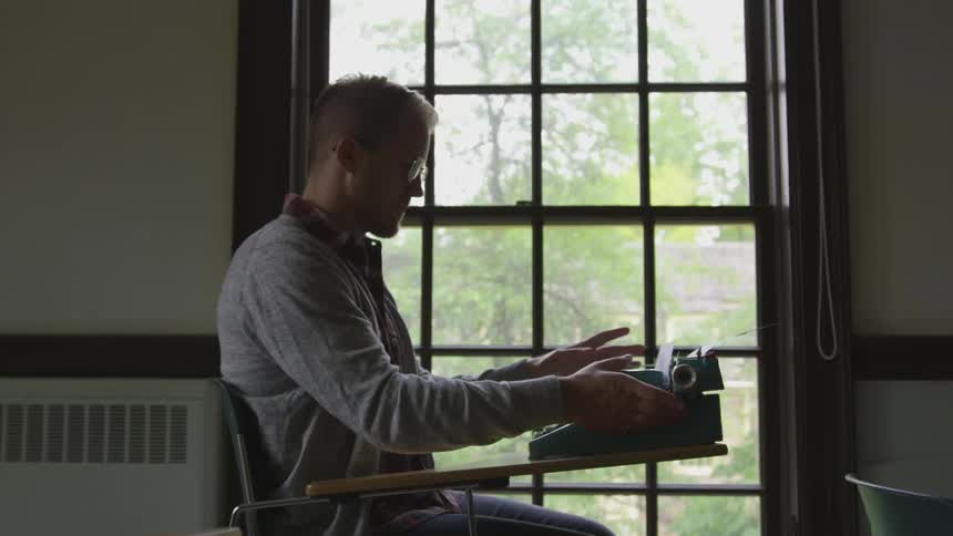 Man at desk types on typewriter