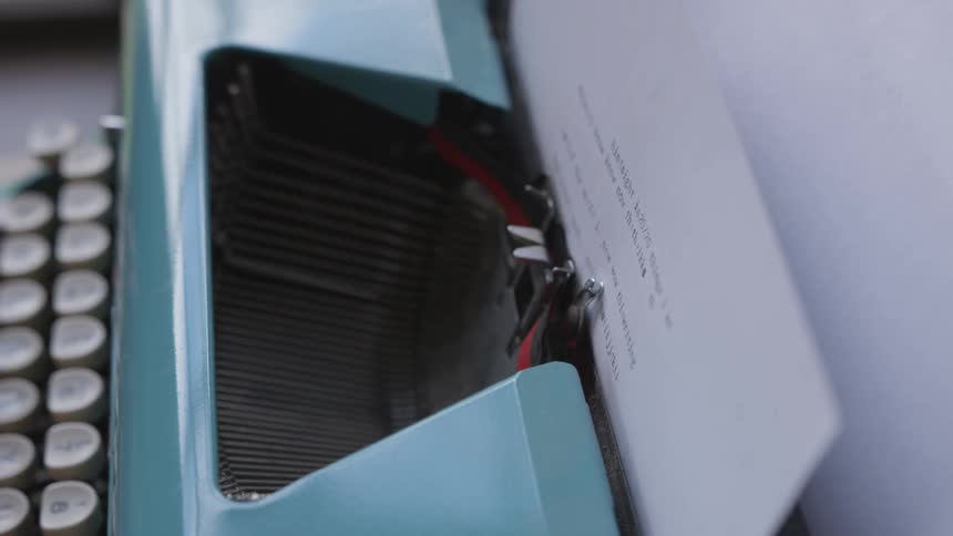 A classic mechanical typewriter is being used by someone to type up something on a piece of paper
